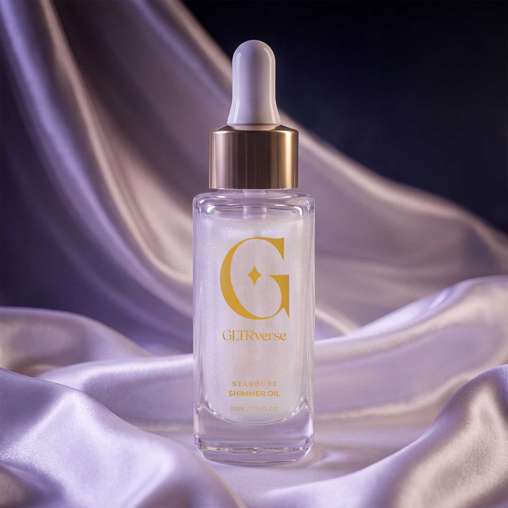 GLTRverse Stardust pearl-white shimmer body oil in a clear glass dropper bottle with a gold collar, on lilac and champagne silk